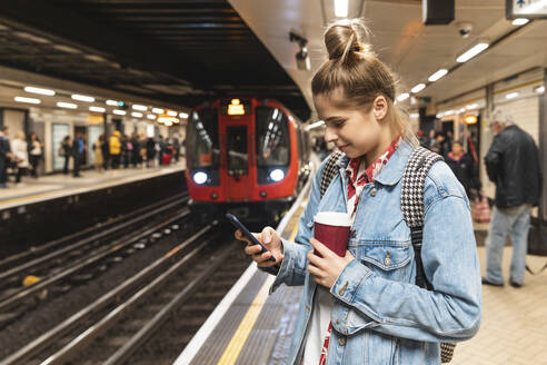 Junge Frau in einer U-Bahn-Station, die ein Smartphone benutzt - WPEF01631