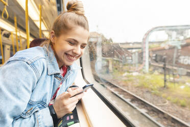 Glückliche junge Frau mit Smartphone bei einer Zugfahrt - WPEF01637