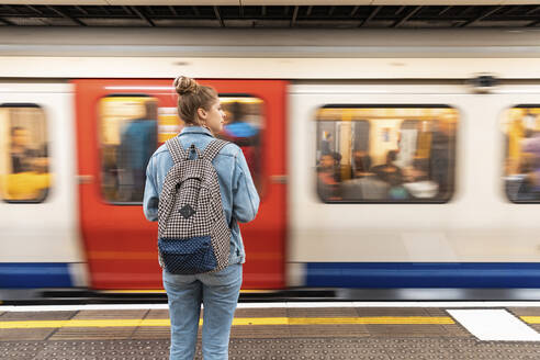 Rückansicht einer jungen Frau in einer U-Bahn-Station mit einfahrendem Zug - WPEF01645