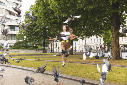 Unbeschwerte junge Frau hat Spaß im Park und jagt Tauben, London, UK - WPEF01653