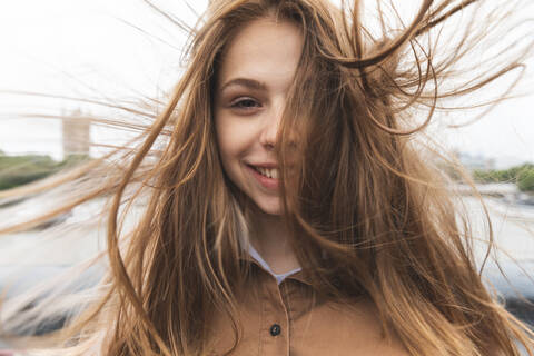 Porträt einer lächelnden jungen Frau mit vom Wind zerzaustem Haar, London, UK, lizenzfreies Stockfoto