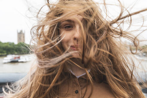 Porträt einer lächelnden jungen Frau mit vom Wind zerzaustem Haar, London, UK - WPEF01655