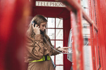 Young woma nmaking a call from a red phone booth in the city, London, UK - WPEF01658