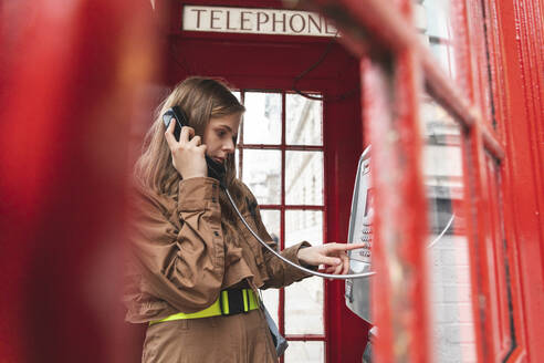 Junge Frau, die einen Anruf von einer roten Telefonzelle in der Stadt tätigt, London, UK - WPEF01658