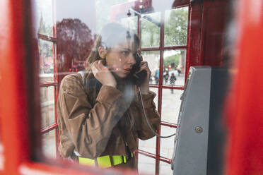 Young woma nmaking a call from a red phone booth in the city, London, UK - WPEF01659