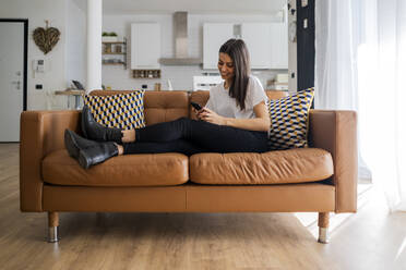 Young woman on couch at home using cell phone - GIOF06916