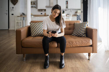 Junge Frau auf der Couch zu Hause, die ein Mobiltelefon benutzt - GIOF06917