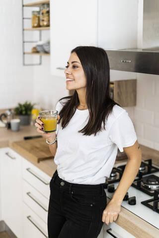 Junge Frau in der Küche zu Hause trinkt ein Glas Orangensaft, lizenzfreies Stockfoto