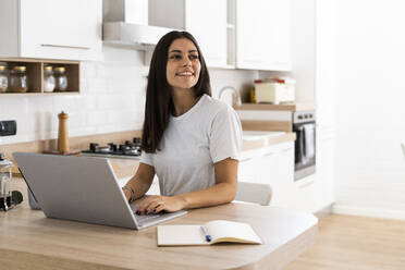 Lächelnde junge Frau, die zu Hause einen Laptop benutzt - GIOF06925