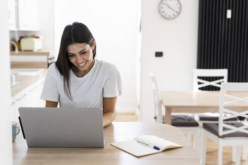 Lächelnde junge Frau, die zu Hause einen Laptop benutzt - GIOF06926