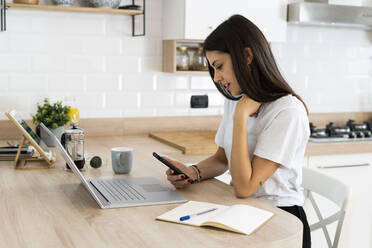 Young woman using cell phone and laptop at home - GIOF06933