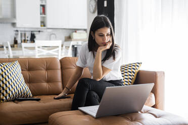 Young woman sitting on couch at home using laptop - GIOF06934