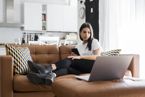 Junge Frau sitzt zu Hause auf der Couch und benutzt einen Laptop, lizenzfreies Stockfoto