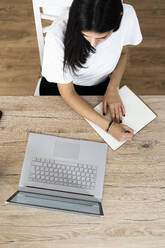 Top view of young woman with laptop taking notes - GIOF06937