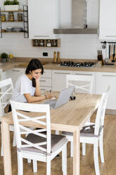 Young woman with laptop taking notes at home - GIOF06940