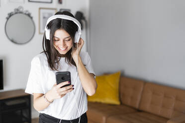 Happy young woman with smartphone and headphones at home - GIOF06954