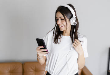 Happy young woman with smartphone and headphones at home - GIOF06955