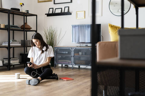 Young woman sitting on the floor at home using cell phone stock photo