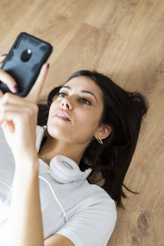 Junge Frau auf dem Boden liegend mit Smartphone in der Hand, lizenzfreies Stockfoto