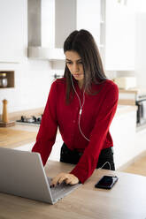 Young businesswoman with earphones using laptop at home - GIOF06967