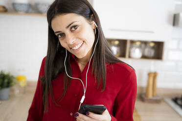 Porträt einer lächelnden jungen Frau mit Kopfhörern und Smartphone - GIOF06969