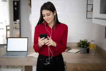 Young businesswoman with earphones using smartphone at home - GIOF06970