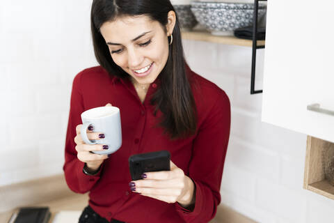 Smiling young businesswoman with cell phone and cup of coffee at home stock photo