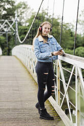 Teenager-Mädchen benutzt Smartphone und hört Musik auf einer Brücke - NMS00360