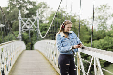 Teenager-Mädchen benutzt Smartphone und hört Musik auf einer Brücke - NMS00361