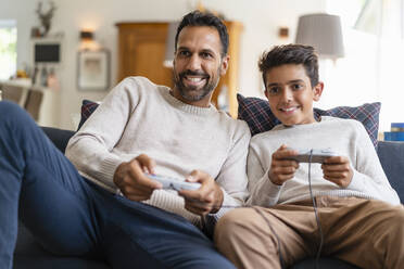 Happy father and son playing video game on couch in living room - DIGF07724