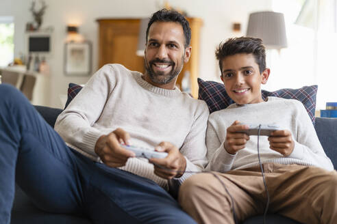 Glücklicher Vater und Sohn spielen ein Videospiel auf der Couch im Wohnzimmer - DIGF07724