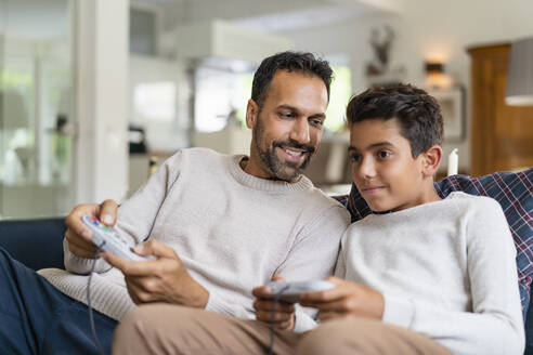 Glücklicher Vater und Sohn spielen ein Videospiel auf der Couch im Wohnzimmer - DIGF07725