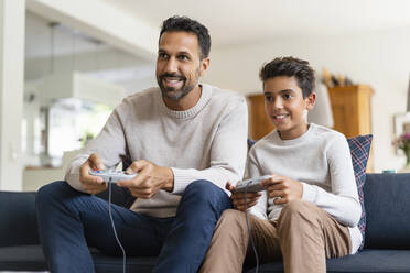 Glücklicher Vater und Sohn spielen ein Videospiel auf der Couch im Wohnzimmer - DIGF07727