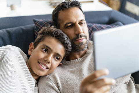 Happy father and son using tablet on couch in living room stock photo