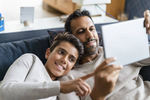 Glücklicher Vater und Sohn benutzen ein Tablet auf der Couch im Wohnzimmer, lizenzfreies Stockfoto