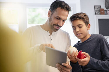 Vater und Sohn benutzen ein Tablet und kochen gemeinsam in der Küche zu Hause - DIGF07738