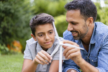 Lächelnder Vater und Sohn liegen im Garten mit einem Windradmodell - DIGF07750