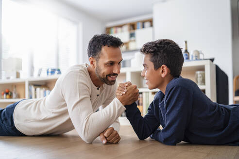 Vater und Sohn liegen zu Hause auf dem Boden und ringen mit den Armen - DIGF07762