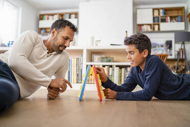 Father and son lying on the floor at home playing a game - DIGF07767