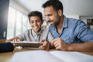 Vater und Sohn benutzen ein Tablet und machen Hausaufgaben - DIGF07787