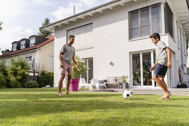 Father and son playing football in garden - DIGF07791