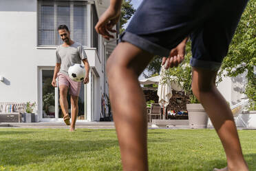 Father and son playing football in garden - DIGF07792