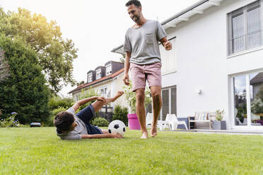 Father and son playing football in garden - DIGF07795