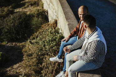 Homosexuelles Paar sitzt auf einer Mauer und hält Hände - LJF00486