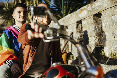 Gay couple with gay pride flag on a motorbike - LJF00487