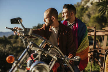 Gay couple with gay pride flag on a motorbike - LJF00488