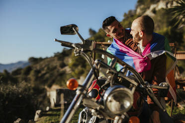 Glückliches homosexuelles Paar mit Homosexuell Stolz Flagge auf einem Motorrad - LJF00490