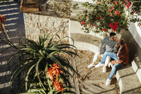 Schwules Paar sitzt auf einer Stufe im Freien, umgeben von Blumen, lizenzfreies Stockfoto
