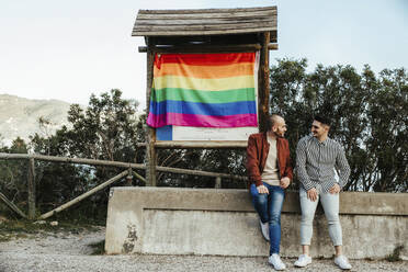 Gay couple with gay pride flag on a trip in the mountains - LJF00495