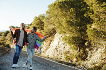 Homosexuelles Paar mit Homosexuell Stolz Flagge zu Fuß auf einer Straße in den Bergen - LJF00501